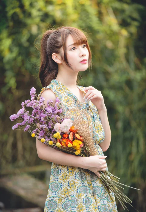 Hình nền ngầu với cô gái trẻ mặc váy họa tiết cầm bó hoa rực rỡ giữa khu vườn xanh mát