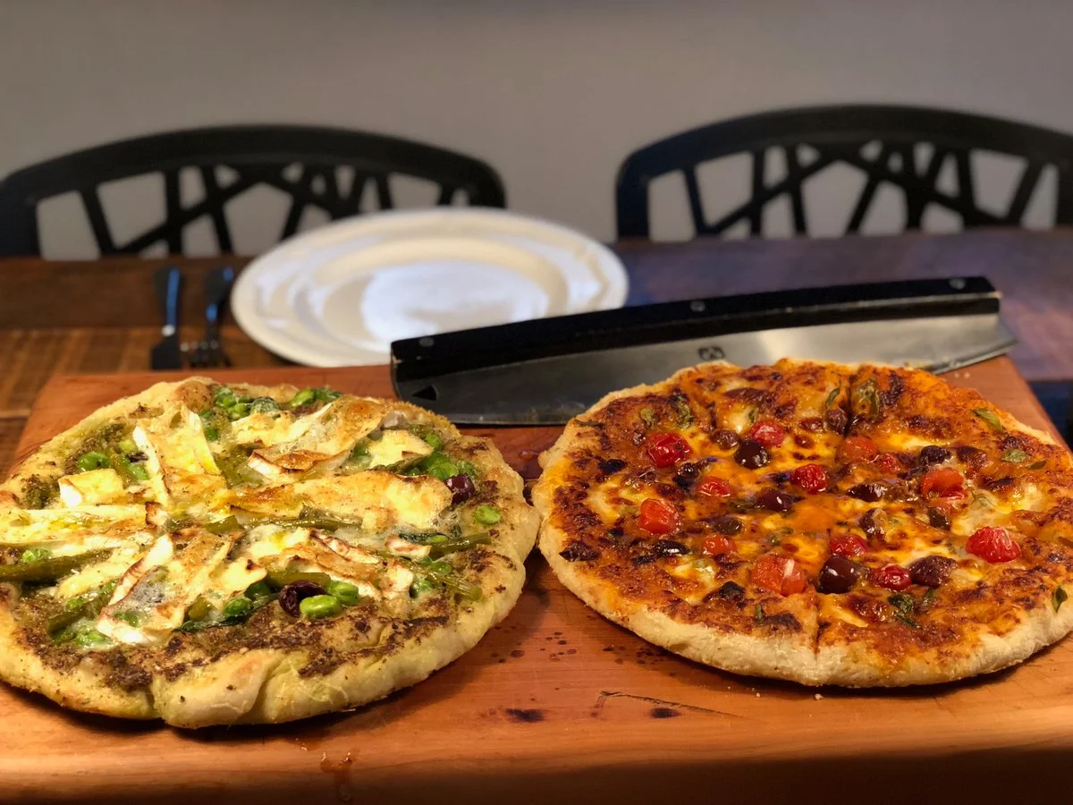 Hai chiếc pizza nướng đặt trên thớt gỗ