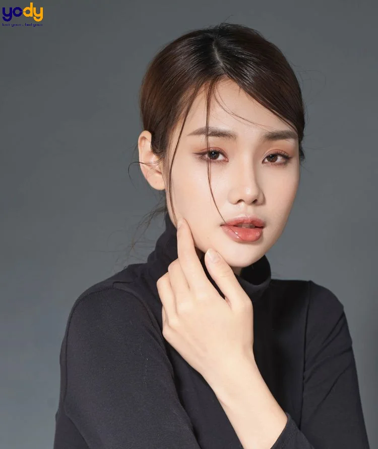 Ảnh chân dung cận cảnh người phụ nữ trẻ mặc áo cổ lọ đen trước phông nền xám