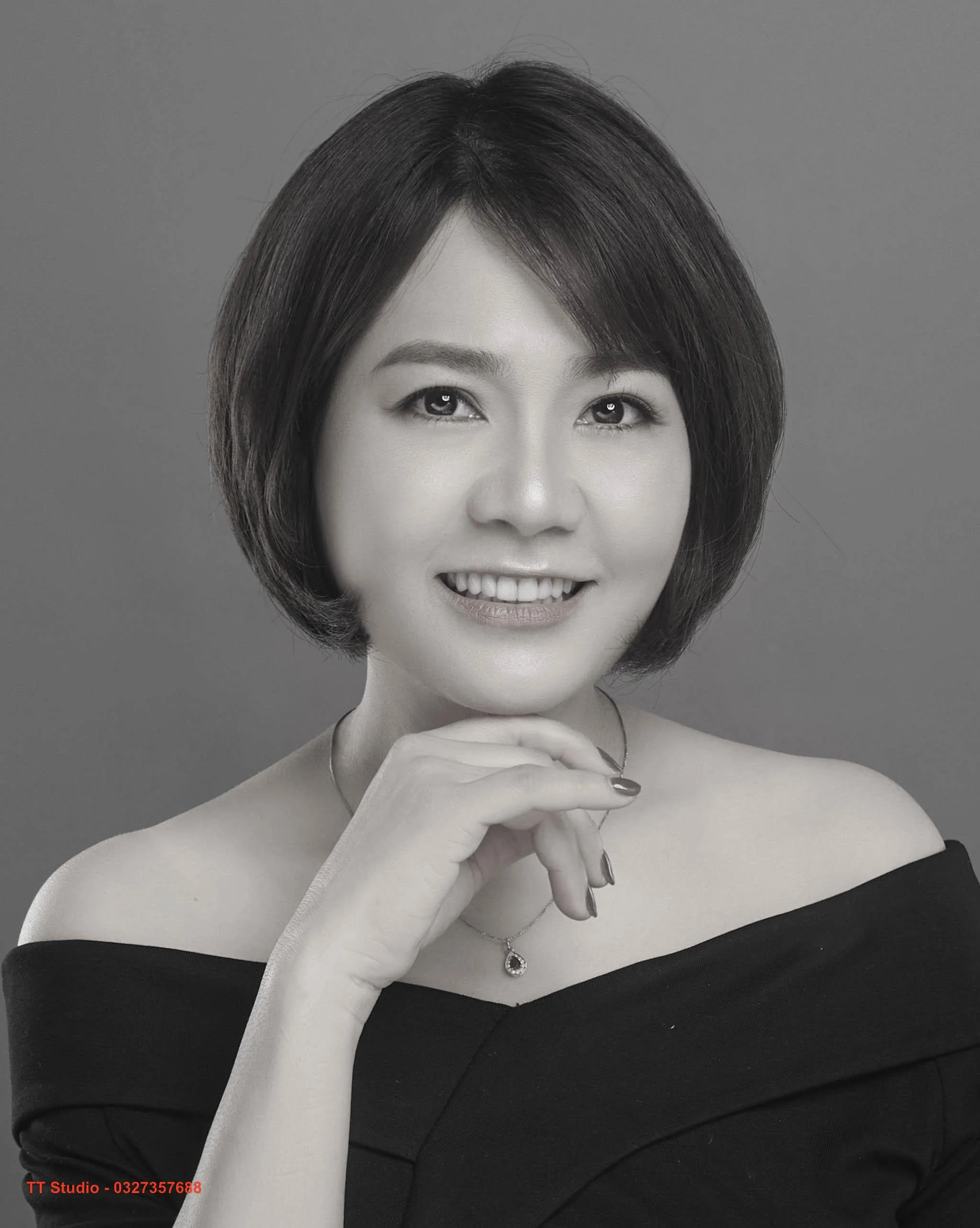 Ảnh chân dung người phụ nữ thanh lịch với mái tóc bob, nụ cười rạng rỡ và trang phục trễ vai trong studio