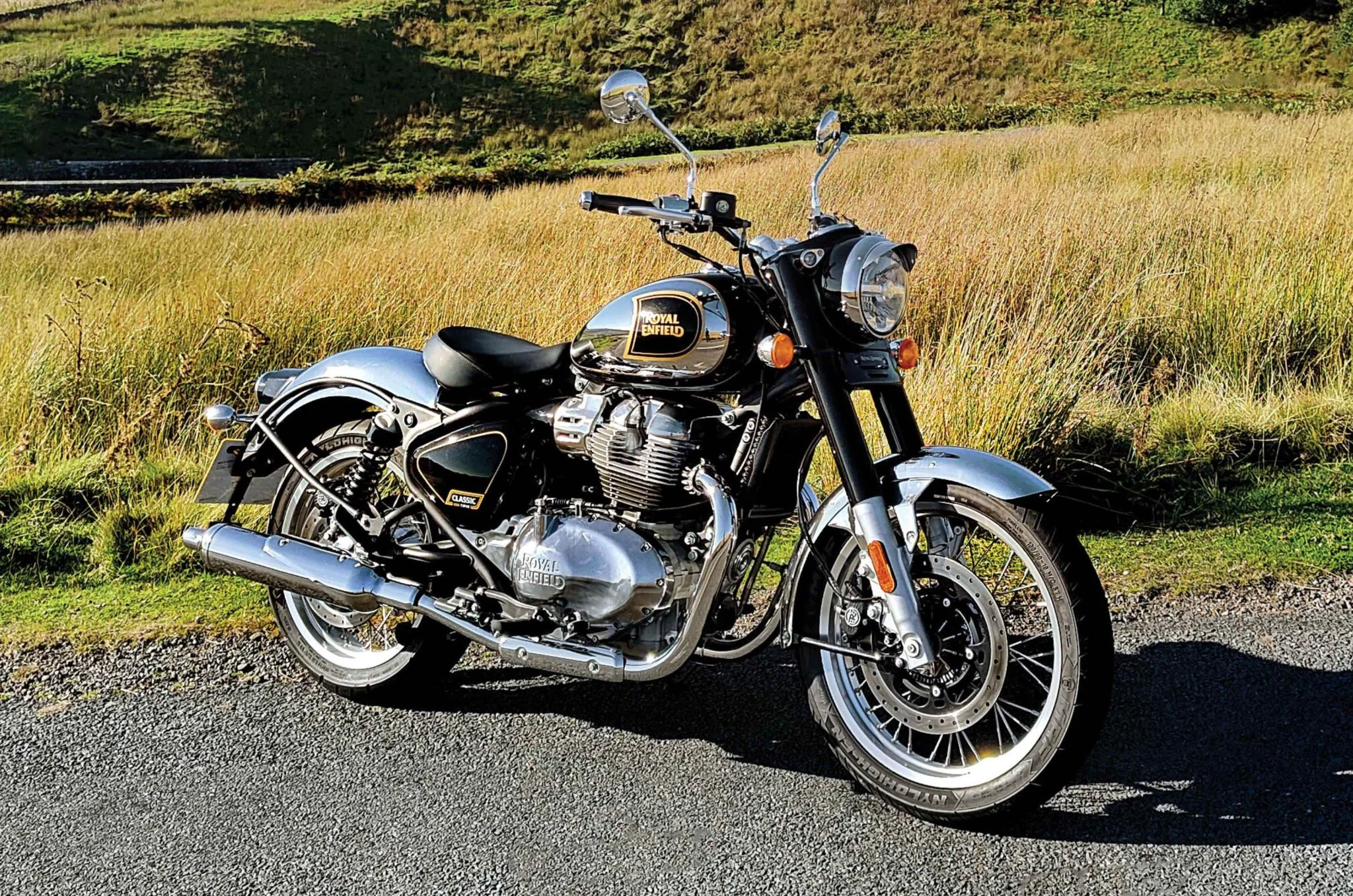 Hình nền đẹp ngầu với xe mô tô Royal Enfield cổ điển màu đen bạc đỗ bên cánh đồng cỏ vàng